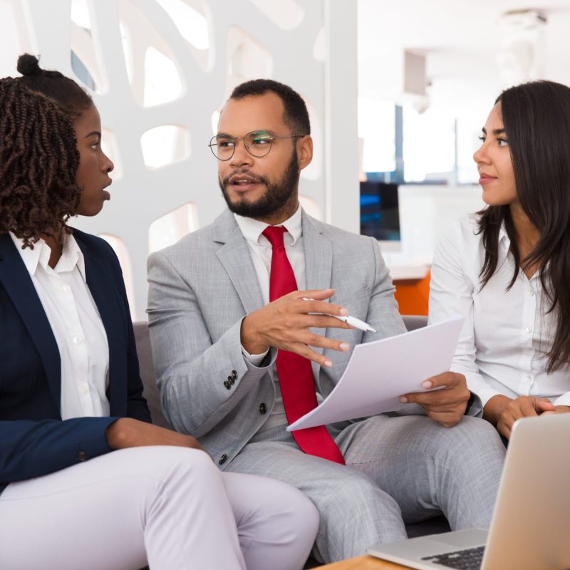Legal expert explaining contract detail to young colleagues. Business man and woman sitting on office couch and discussing document. Document expert concept