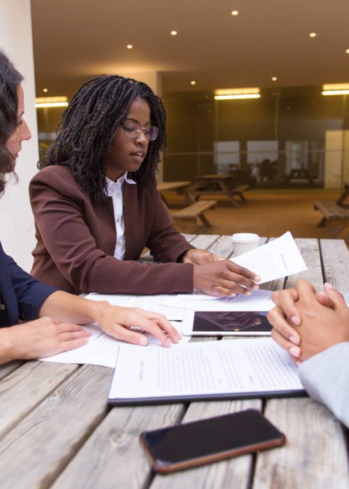 Business partners consulting legal expert in outdoor cafe. Business man and women sitting at table outside, checking and discussing documents. Expertise concept
